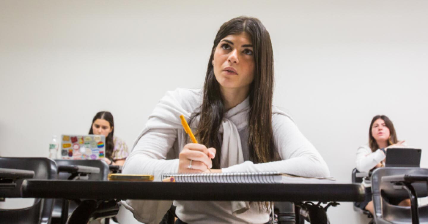 A female Yeshiva University student is sitting in class while taking lecture notes.