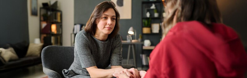 Female mental health counselor sitting opposite to client, holding hands in supportive gesture during a session