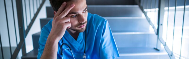 Tensed male nurse sitting on hospital staircase.