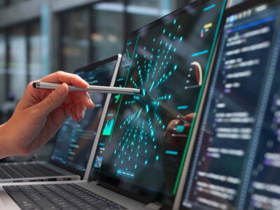 A woman's hand holding a stylus—pointing it at the center of a laptop screen.