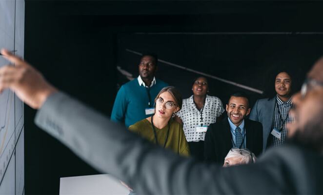 Professor pointing to whiteboard in front of diverse group of students