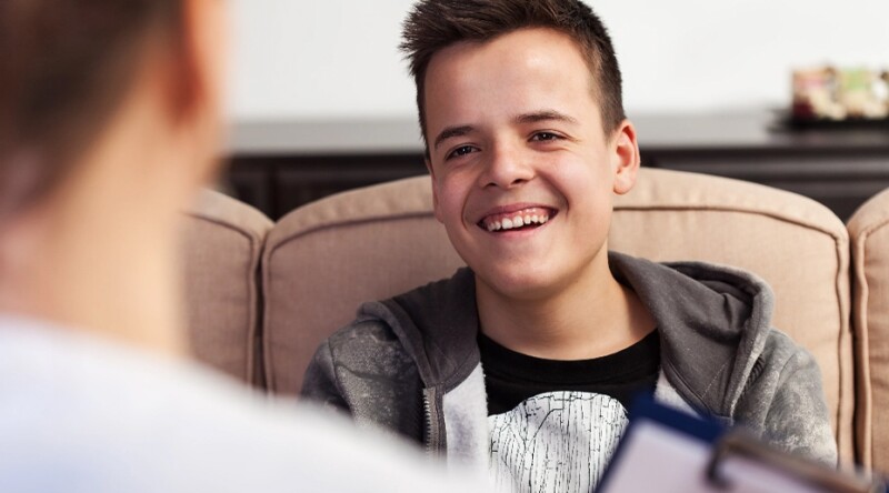 Young male in hooded sweatshirt smiling and speaking to counselor