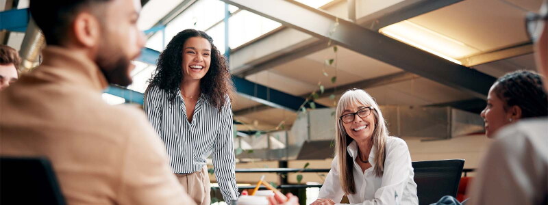 A diverse group of people smiling and collaborating during a meeting in a bright, modern office space.