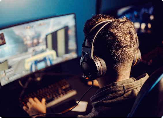 Person wearing headphones playing a video game on a computer in a dimly lit room.