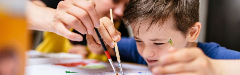 Young female teacher explain, talk at desk with an autistic schoolboy.