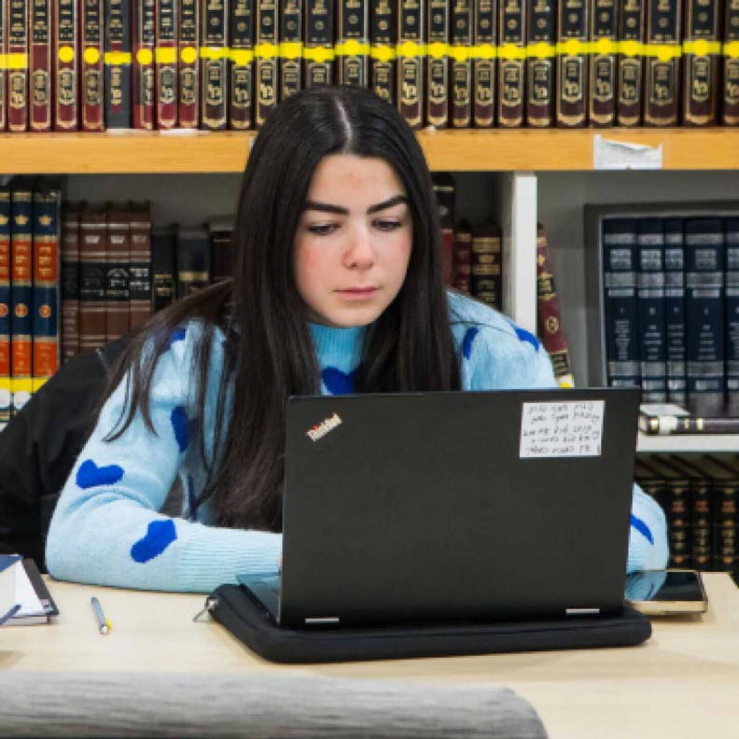A female student works on her laptop while sitting in the campus library.