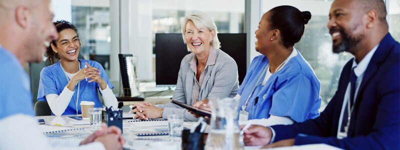 A group of smiling healthcare professionals seated at a table in front of documents.