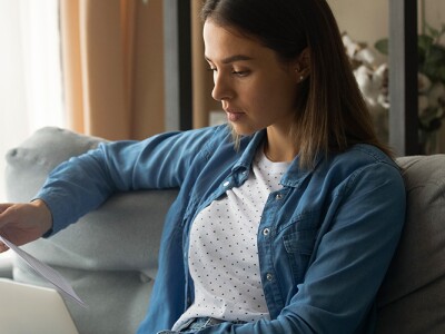 Woman sitting on a couch with laptop and looking over paperwork