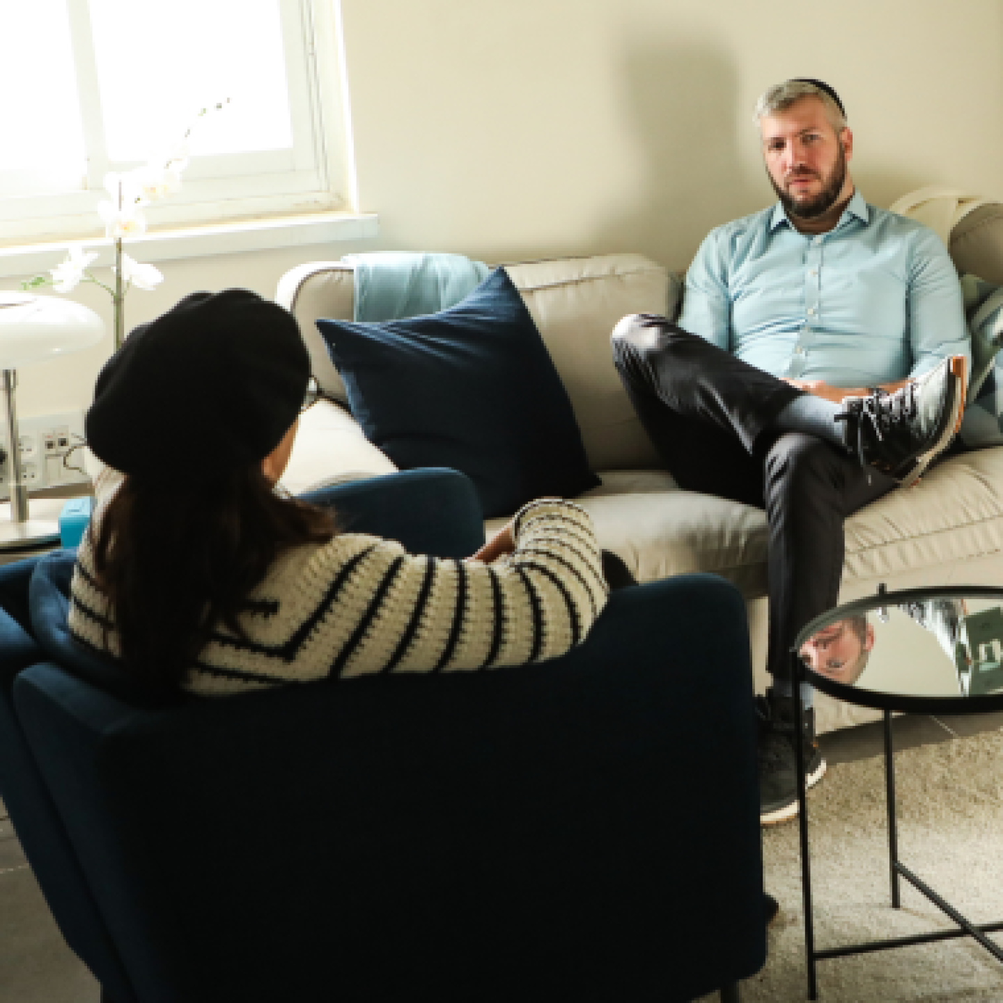A young female sits in a chair while talking with a male on a couch.