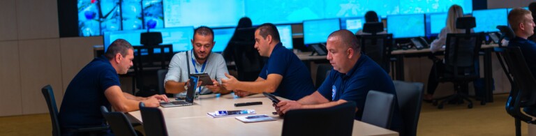 Team sits around a table reviewing laptop and tablets