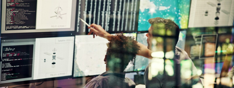 A man and a woman sit before a wall of screens, reviewing data.