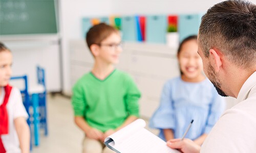 smiling kids sitting in a classroom with a school counselor