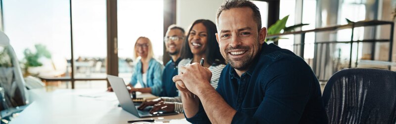 Smiling mature businessman sitting with colleagues in an office.
