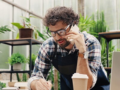 Happy caucasian male florist calling on smartphone at work.