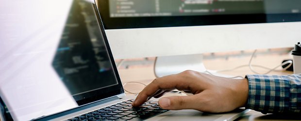 close-up-of-man's-hand-on-laptop-with-desktop-monitor-in-background