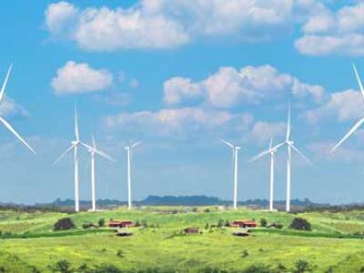 Windfarm windmills stand over meadows on a sunny, slightly cloudy day.