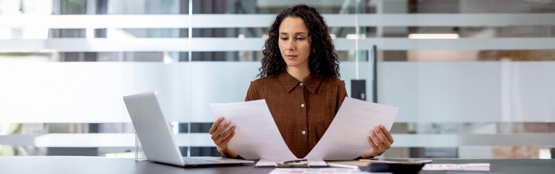 Woman at her desk comparing two financial documents.