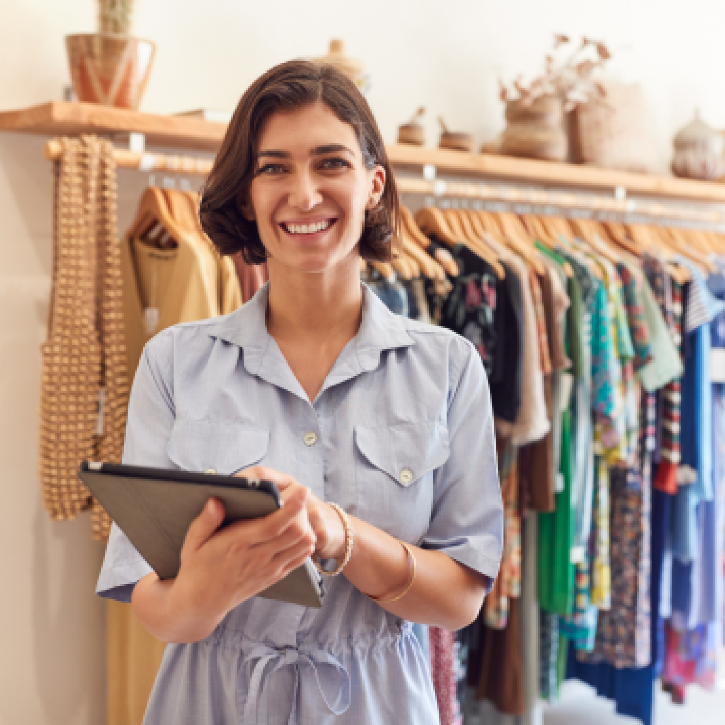A female entrepreneur is holding a table while standing in front of a clothing rack.