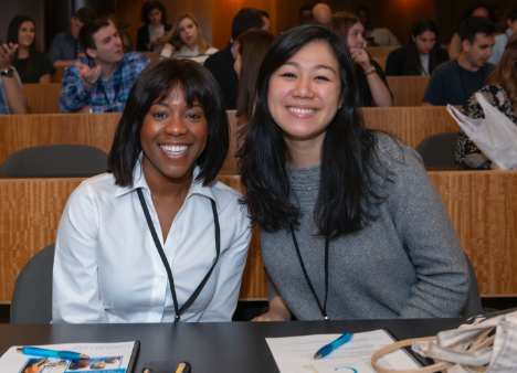 two students pose for a photo in class while others participate in break-out discussions