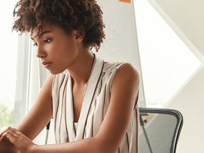 woman sitting at computer in beige shirt beige abstract wall behind her
