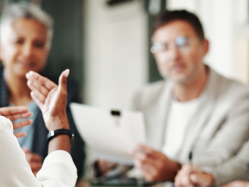 A woman with her back to the camera explains a concept to three other professionals.