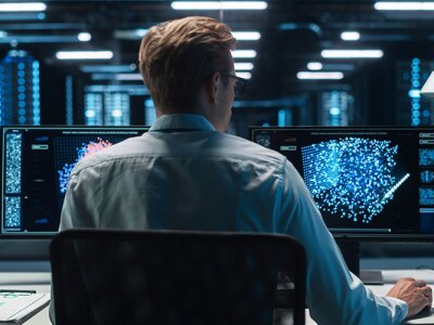 cybersecurity analyst sitting at a desk monitoring two screens