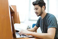 man with dark hair and black beard with headphones on working on computer