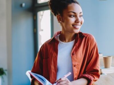 woman-with-hair-up-in-orange-shirt-smiling-looking-to-side-in-blue-room
