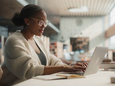 Female Student Engaged in Online Learning at a Modern Library.