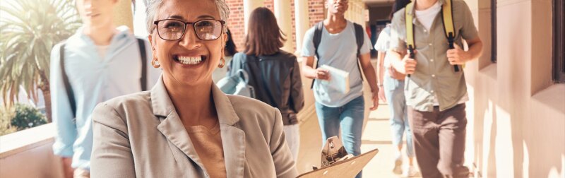 Closeup of school principal smiling in a hallway, while students walk in the background.