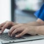 A healthcare professional is typing on a laptop, updating medical records, and conducting research.
