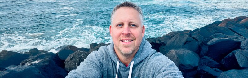 Brian Gordon, KU Professor, standing on rocks next to the ocean.