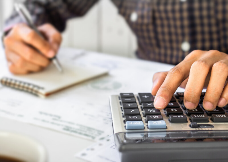 Close up of hands using a calculator and writing on a note pad