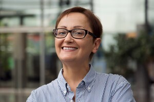 Professional headshot of a confident female teacher standing in front of school.