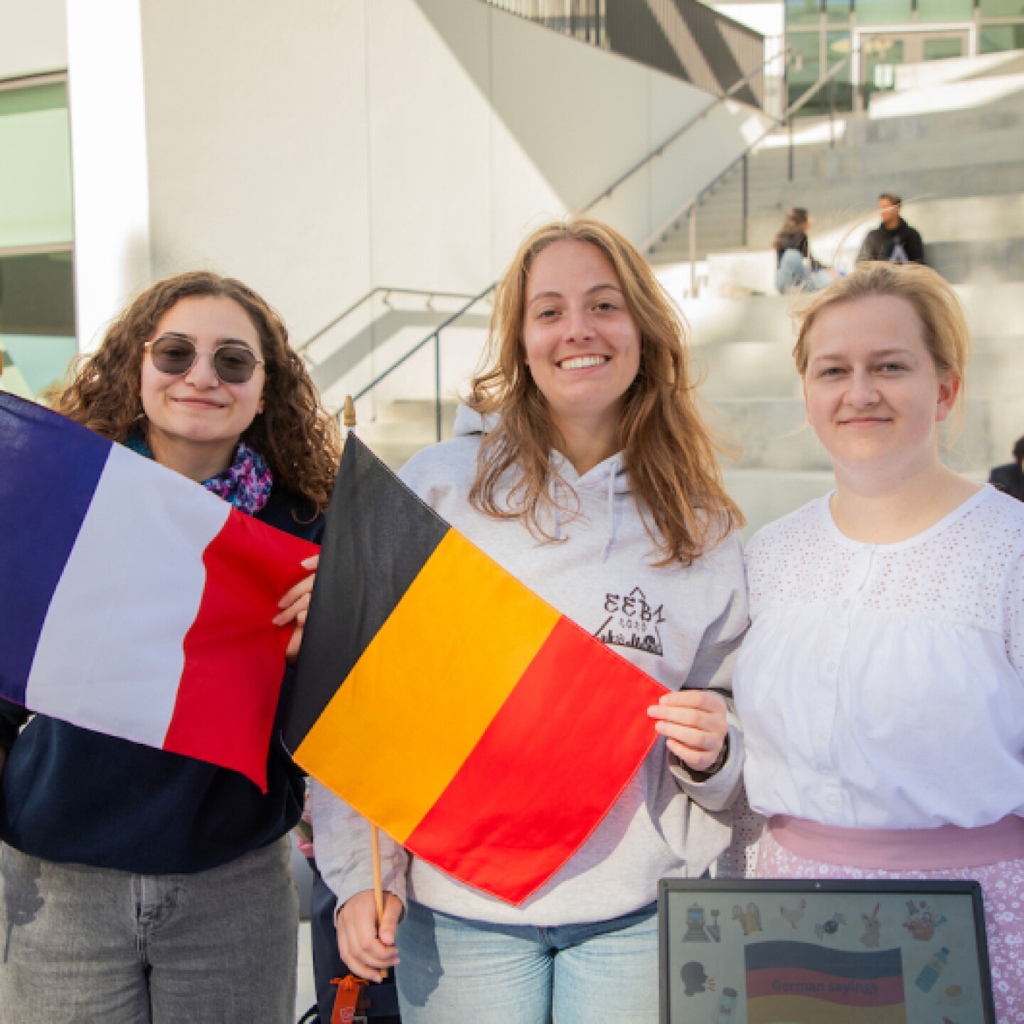 A group of female CSUMB students smiling while holding French and Belgian flags on campus.