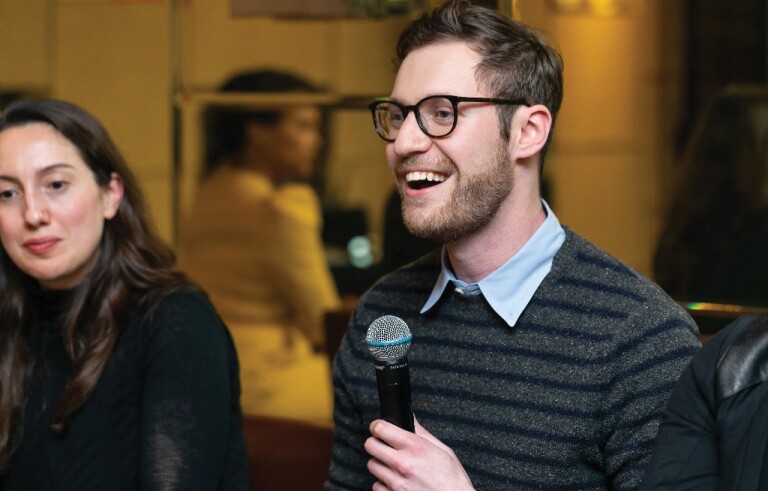 Man in sweater and glasses speaking into microphone