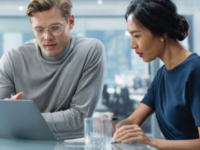Two people sitting at a table looking at a laptop.