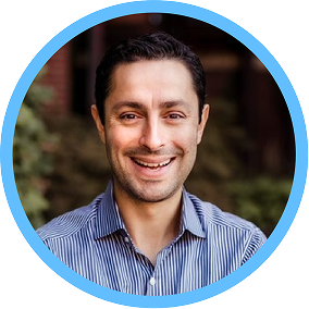 A headshot of Ali Yildirim, Chief Marketing Officer at Iowa, smiling and wearing a blue striped shirt. The image is framed within a circular blue border, with a blurred outdoor background.
