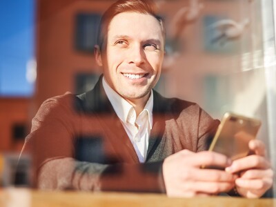 Male with phone in hand sitting in cafe, reflection of building in glass