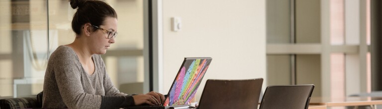 A student sits at a table working on her laptop
