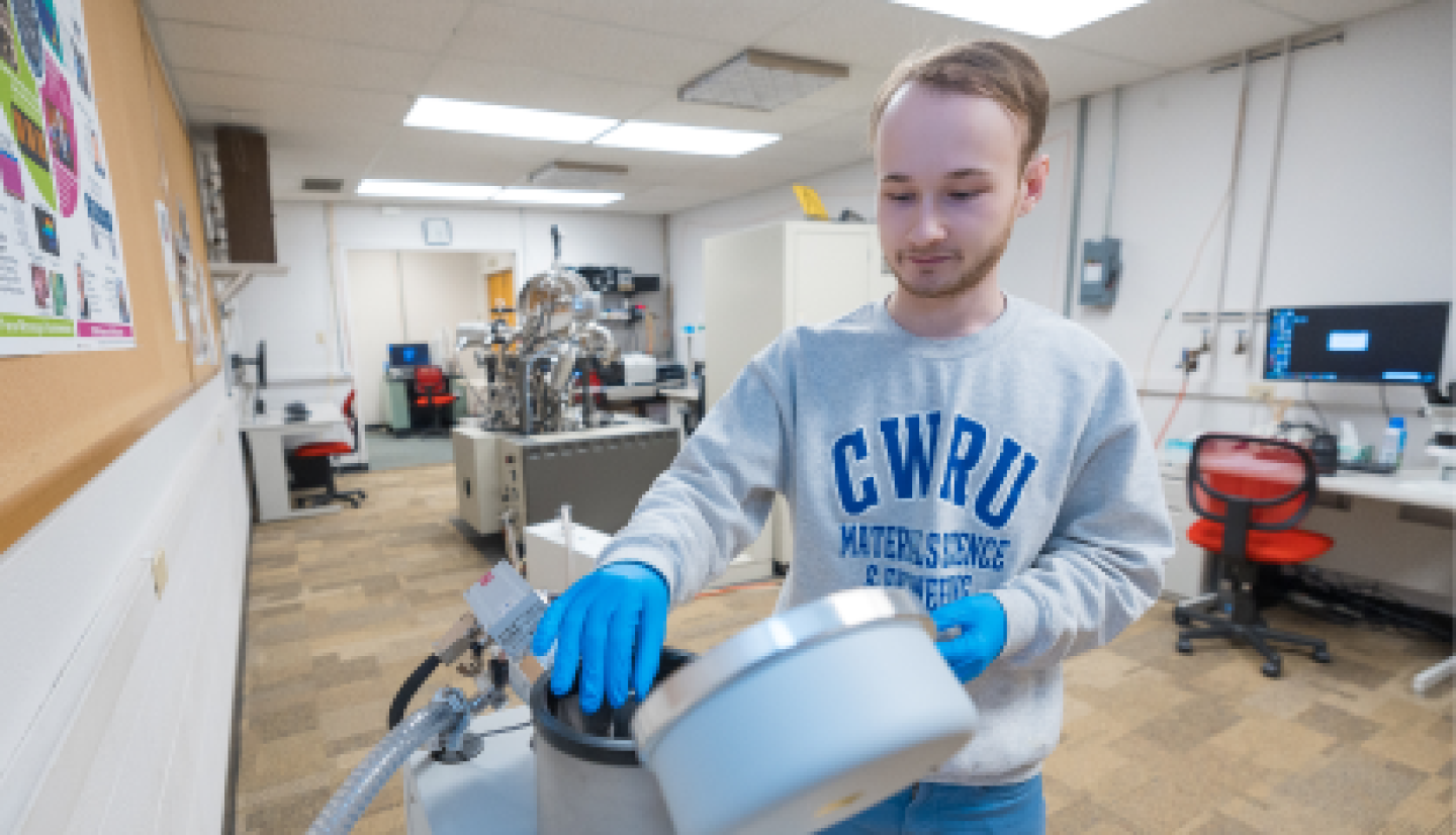 A male CWRU student attaching feed drum to calibration device in fabrication workshop.