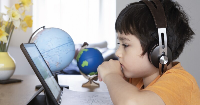 Boy in yellow shirt watching laptop globes in the background