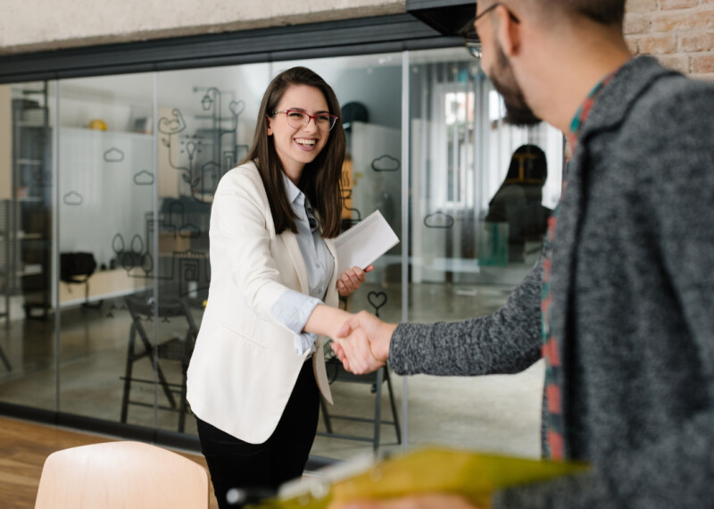 Woman in white blazer shakes hands with man in gray blazer