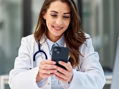 Female doctor sitting at the office table in front of the laptop and using a mobile phone