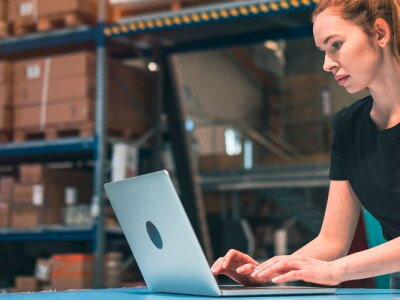 Female warehouse manager using laptop to review shipping data.