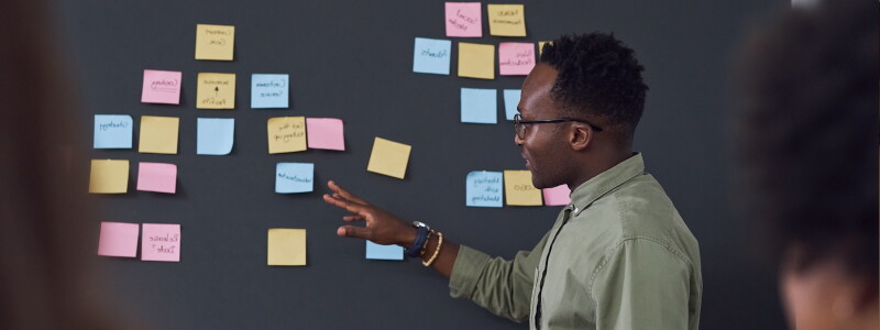 Man stands in front of a chalk board reviewing curriculum plans in a faculty staff meeting