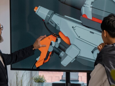 Two men review a design for a game device on a big screen in an office.