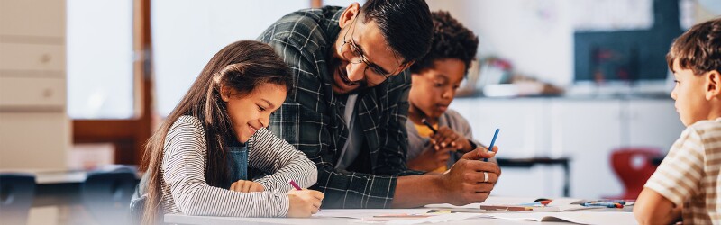 Male teacher mentoring elementary student in class