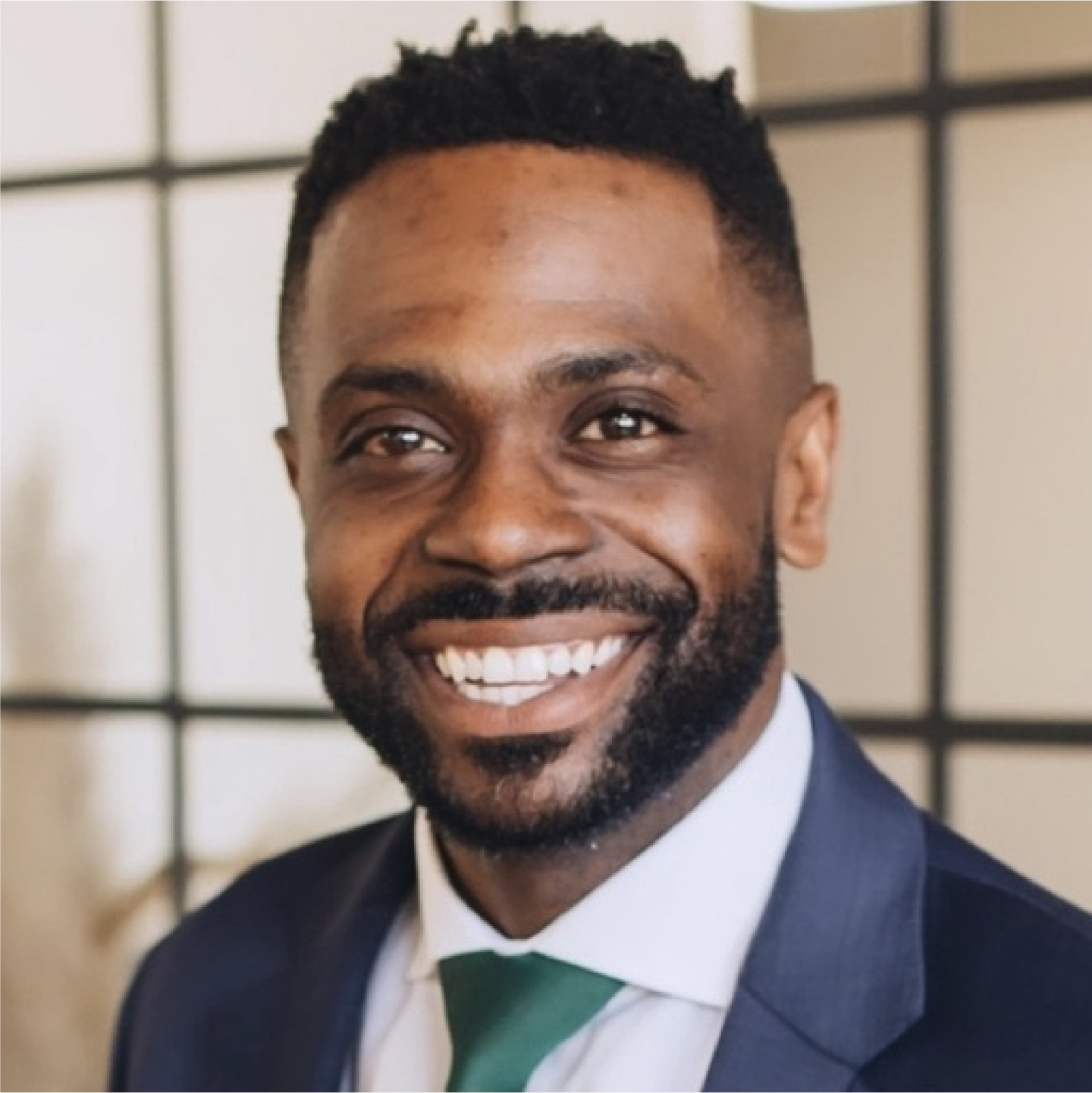 Professional headshot of Cameron Merritt with short hair and a trimmed beard, wearing a suit and green tie against a soft indoor background.