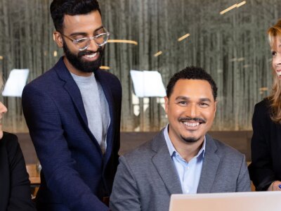 Colleagues gather around a smiling marketer while discussing marketing strategies.